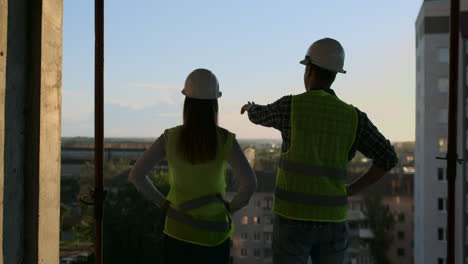 Builders-look-at-a-cityscape-on-a-sunset-background-back-view.